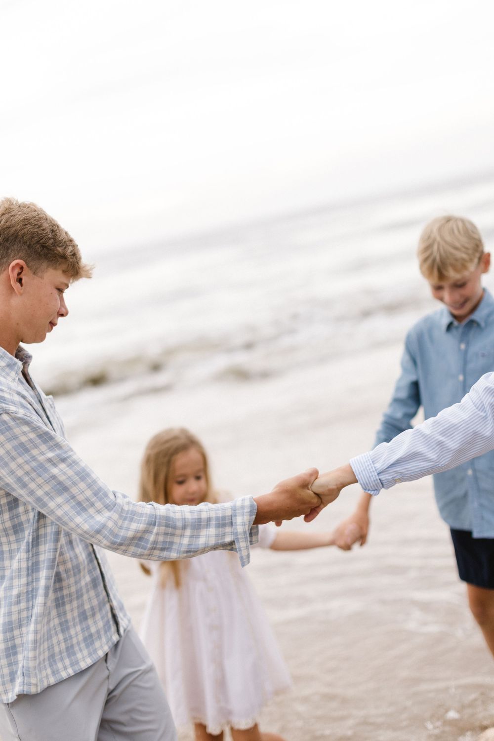 Children hold hands while playing together on a sandy beach.