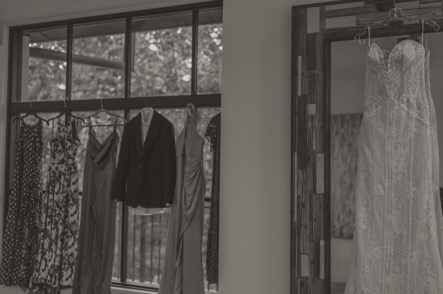 Black and white photo by samantha campbell of wedding attire displayed in a venue, with tuxedo and white gown visible on windows.
