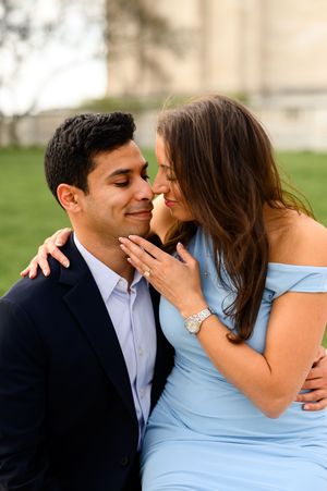 Couple sharing a romantic moment outdoors, woman in blue dress touching mans face, engagement photo session.
