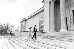 Couple walking down grand museum steps in black and white engagement photo with tall columns backdrop.