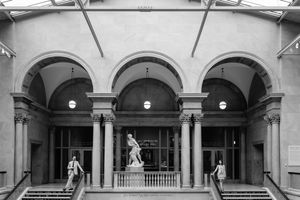 Black and white photo of a classical building entrance with arched colonnade, statues, and grand staircase.