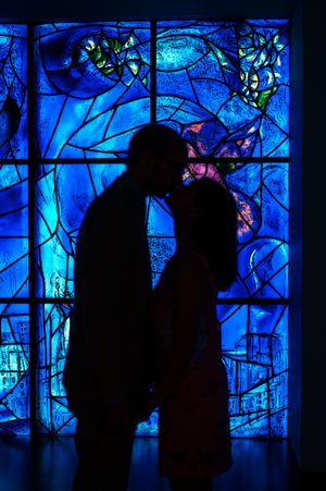 Romantic couple silhouette kissing in front of vibrant blue stained glass window artwork.