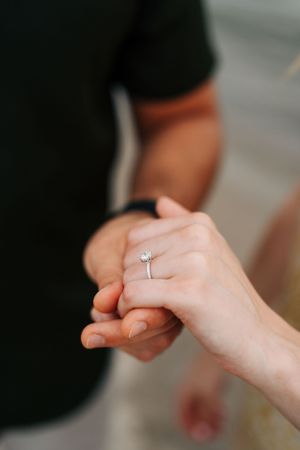 Close-up of two hands holding together with a diamond engagement ring visible.