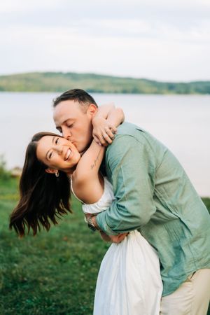 A romantic outdoor photoshoot by a lake with scenic rolling hills in the background.
