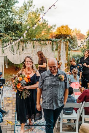 Fall outdoor wedding ceremony with macrame backdrop and floral decorations during recessional at sunset.