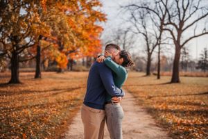 A couple embraces on a path surrounded by fall foliage and orange autumn leaves in a park.