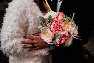 A delicate bouquet of pink and peach roses held against a fluffy white textured garment in dramatic lighting.