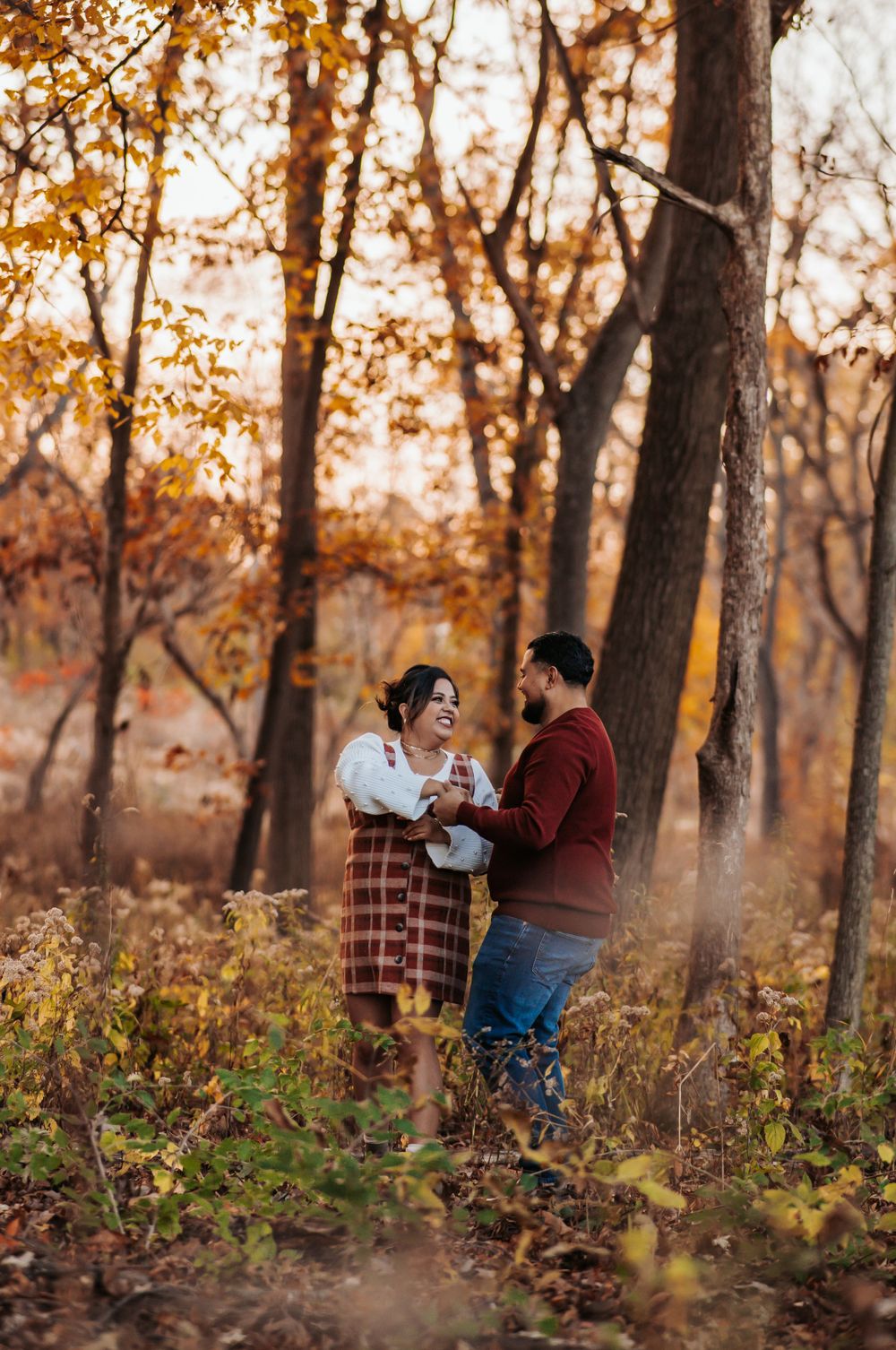 A couple shares a tender moment together in an autumn forest with golden foliage and glowing sunlight in the background.