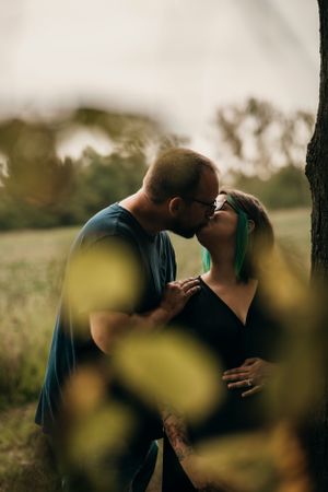 A romantic couple shares a tender kiss in a sunlit field during golden hour, with soft bokeh in the foreground.