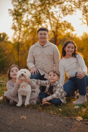 A family sits together outdoors during golden hour autumn sunset with their small white puppy.