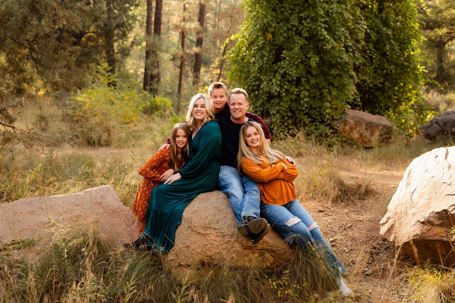Family portrait of five with colorful outfits while posted sitting on a cool boulder in a green forest located in Prescott Arizona.