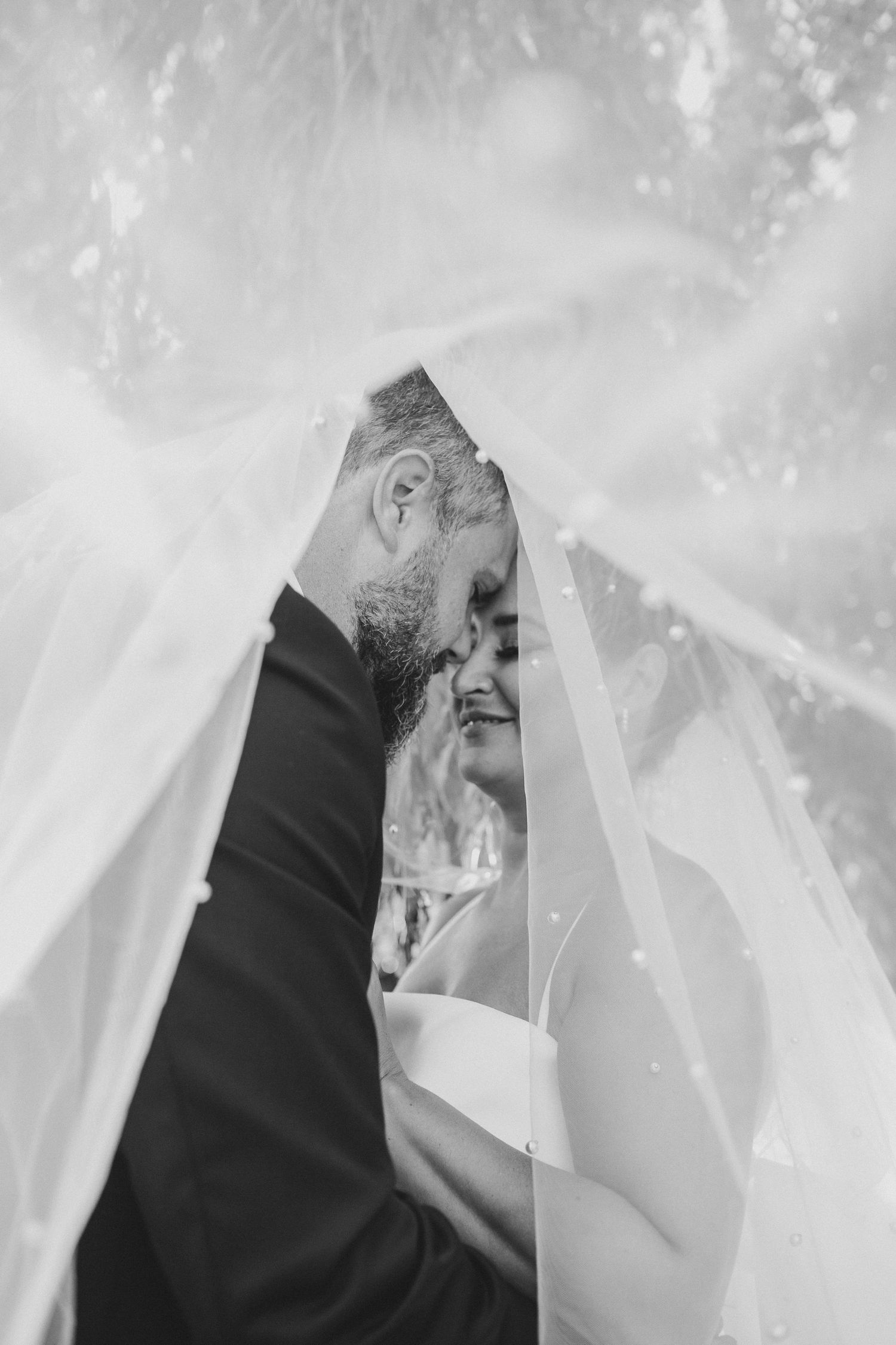 Romantic black and white photo of a couple sharing an intimate moment under a wedding veil.