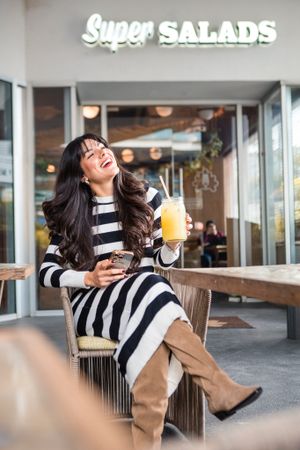 A person in a striped dress enjoys a drink outside Super Salads restaurant.