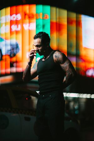 Person in black tank top poses against colorful striped backdrop with vibrant orange and teal lighting effects.