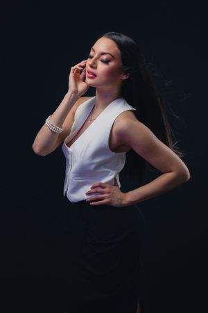 Elegant fashion pose in white sleeveless top against dark background with dramatic lighting.