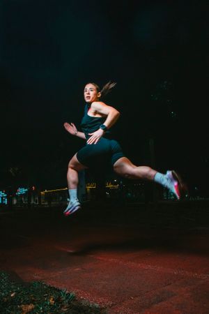 Athletic person in dark athletic wear jumps dynamically at night on an illuminated urban street.