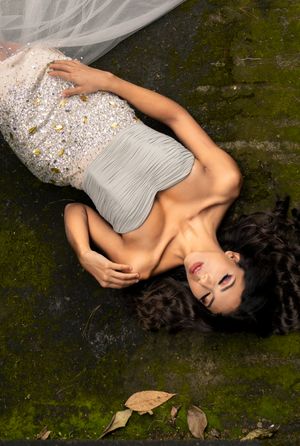 Artistic portrait of woman in sparkly dress lying on mossy ground with delicate veil.