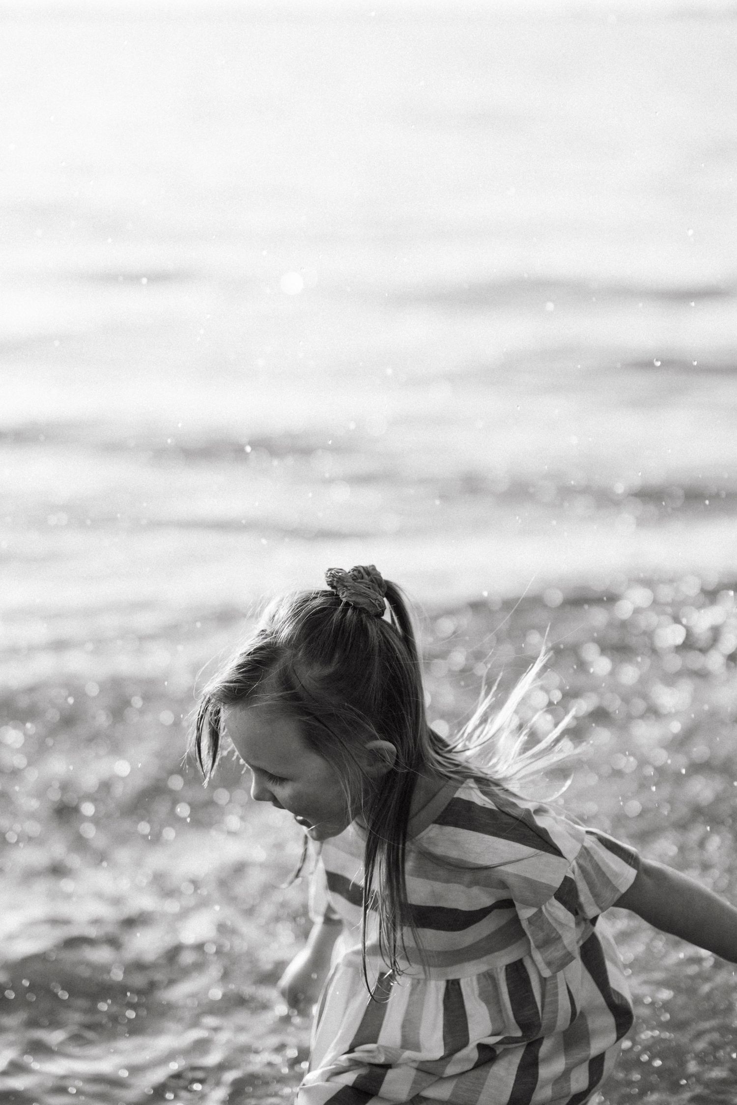 Black and white portrait of young girl playing in ocean waves at the beach.
