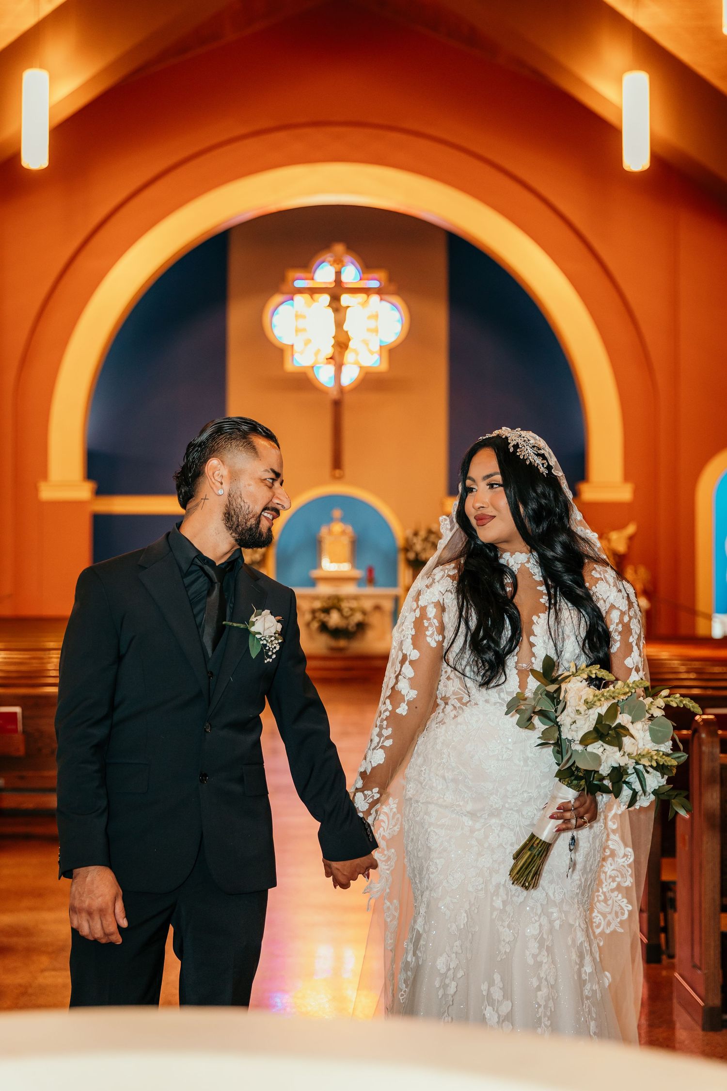 A romantic wedding couple shares a tender moment in the fog while holding a bouquet of red and white flowers.