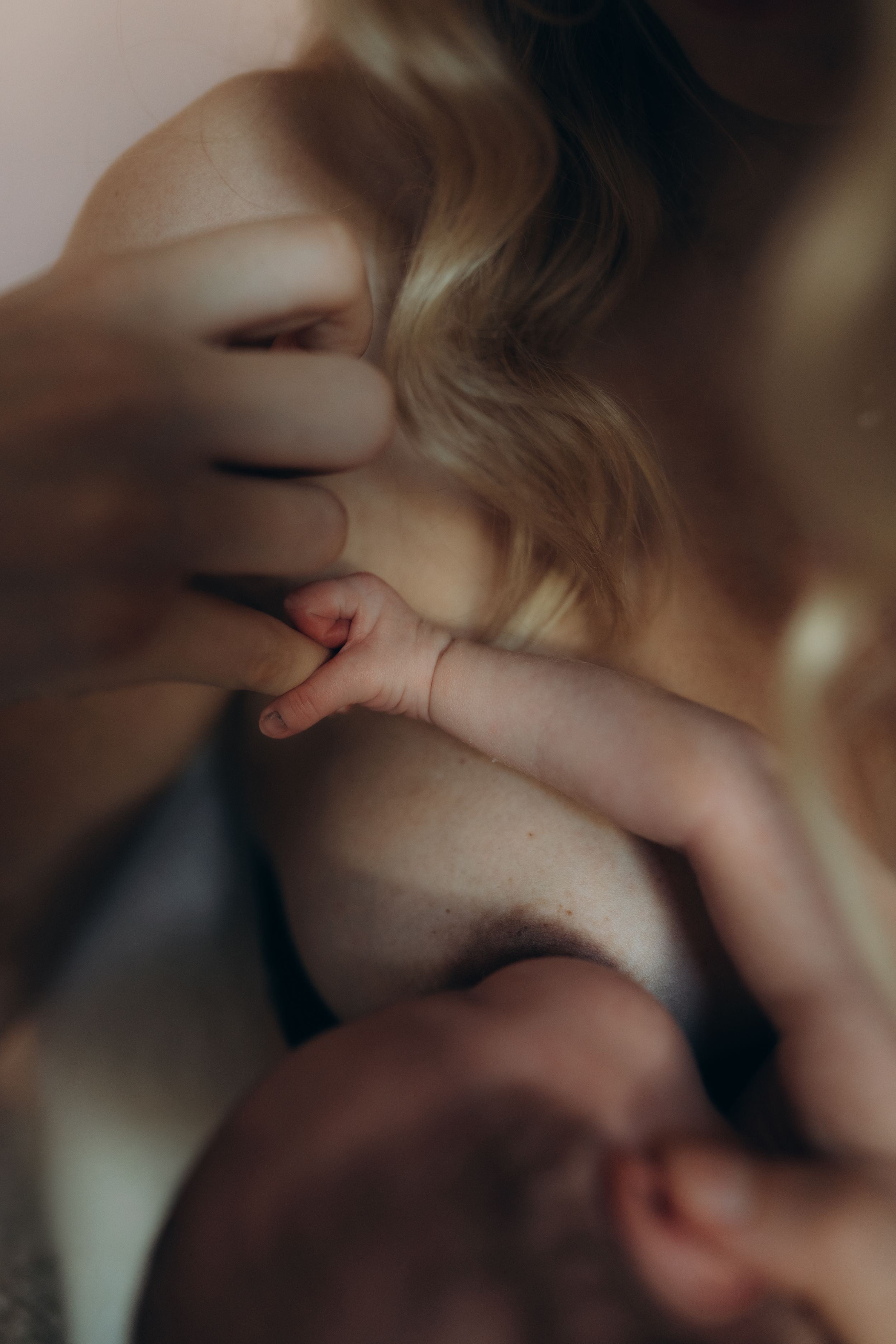 A close up of a new-born's hand holding her mother's finger while nursing during a maternity photo session in London