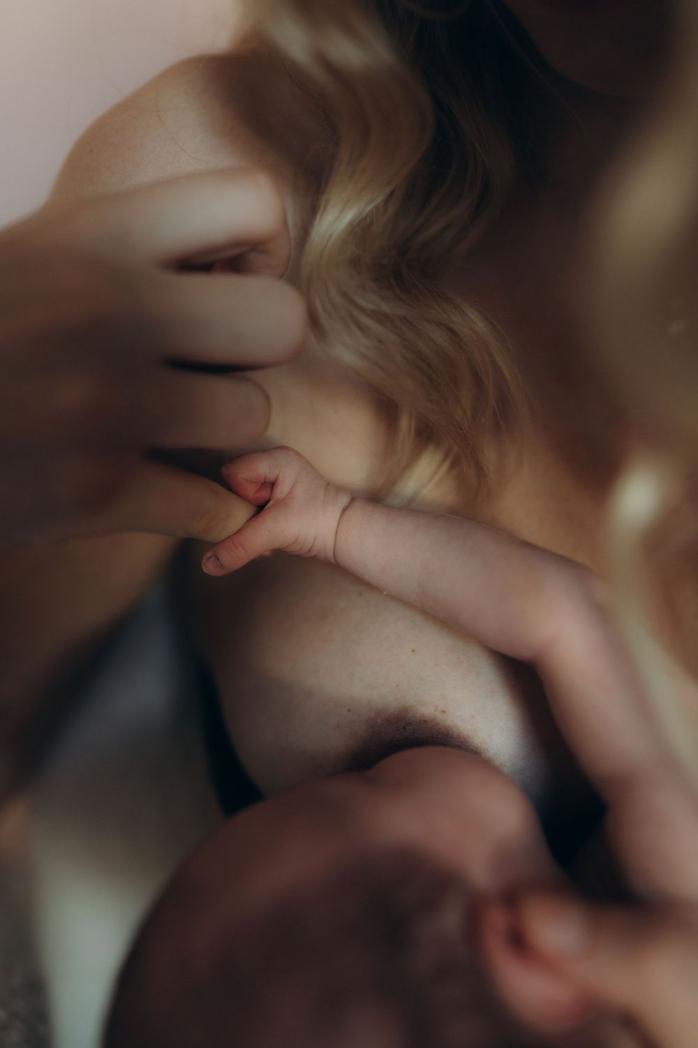 A close up of a new-born's hand holding her mother's finger while nursing during a maternity photo session in London