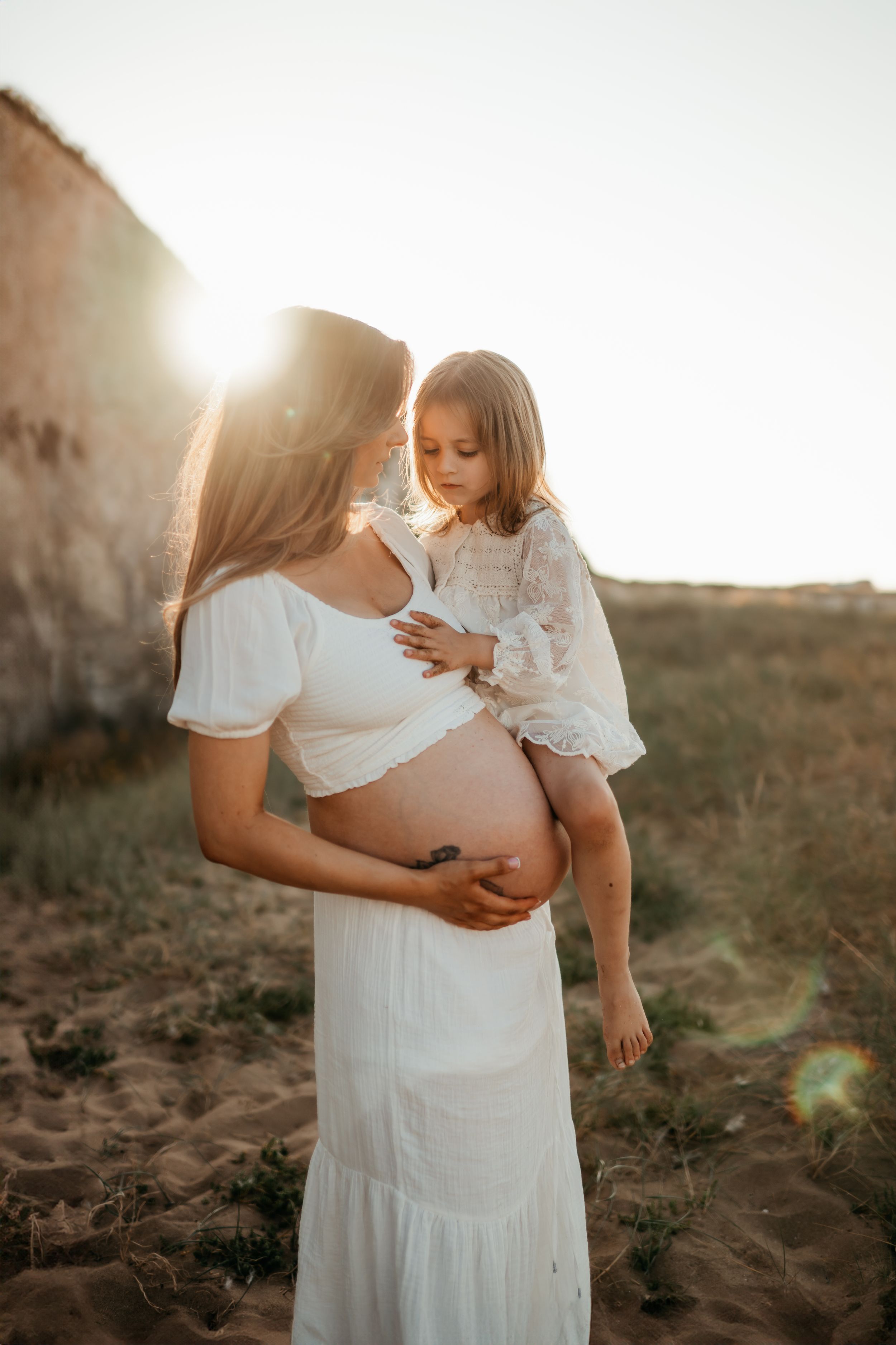 A pregnant woman holding her daughter in her arms during a family photo session in Kent
