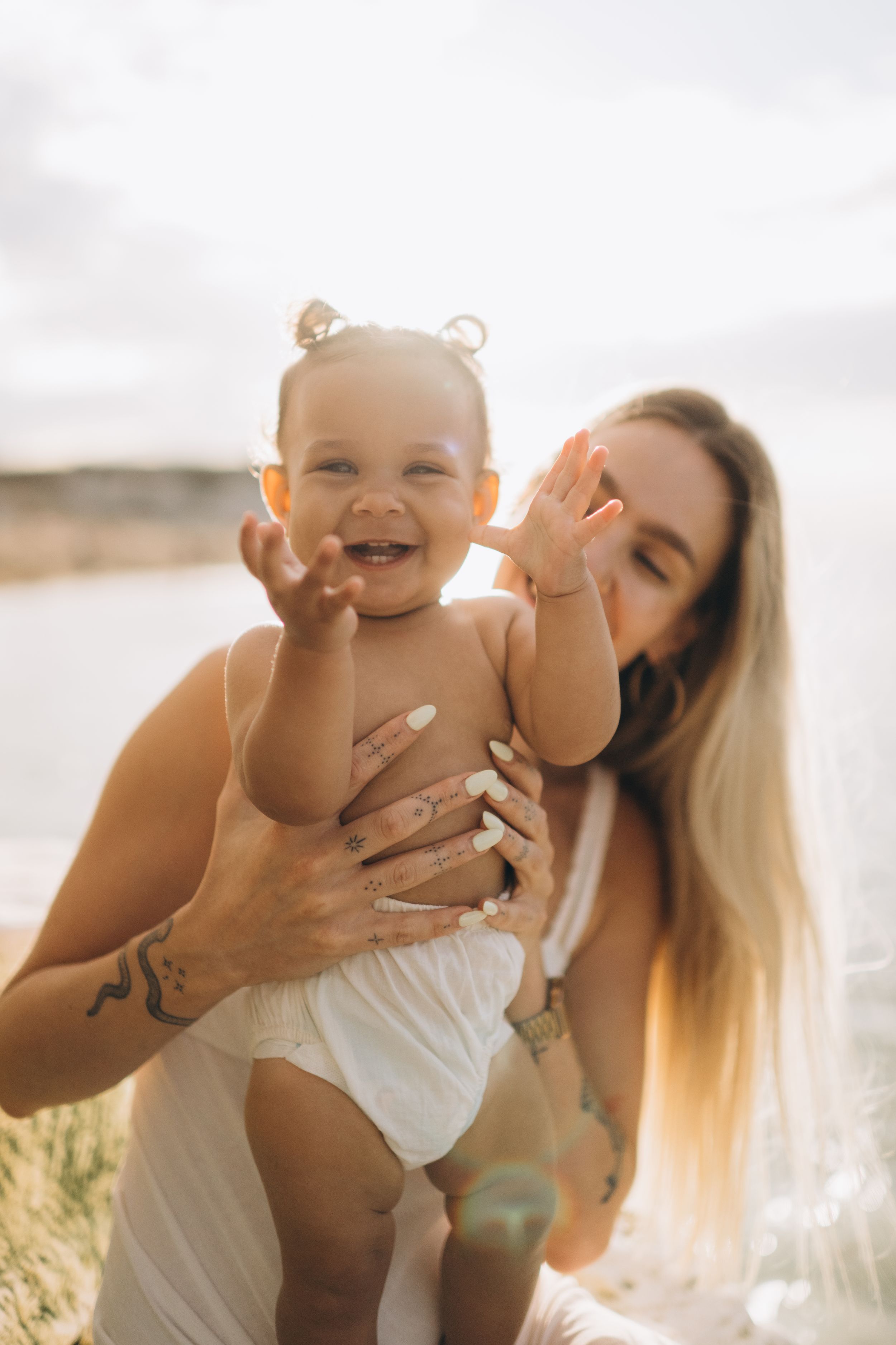 a little girl laughing and clapping hands while being held by her mother on the beach during a family photo session in Kent