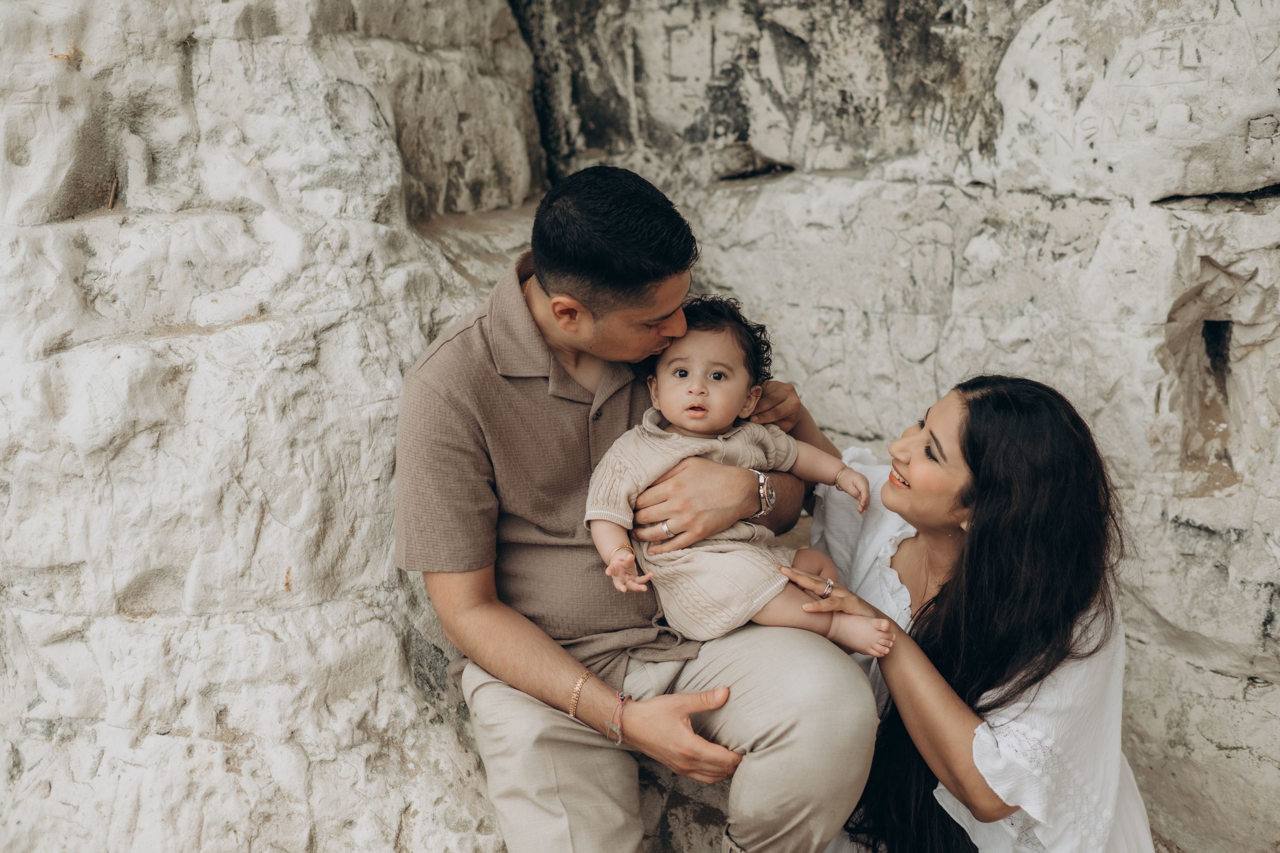 A family of three sitting on the white cliff beach during their family photo session in Botany Bay