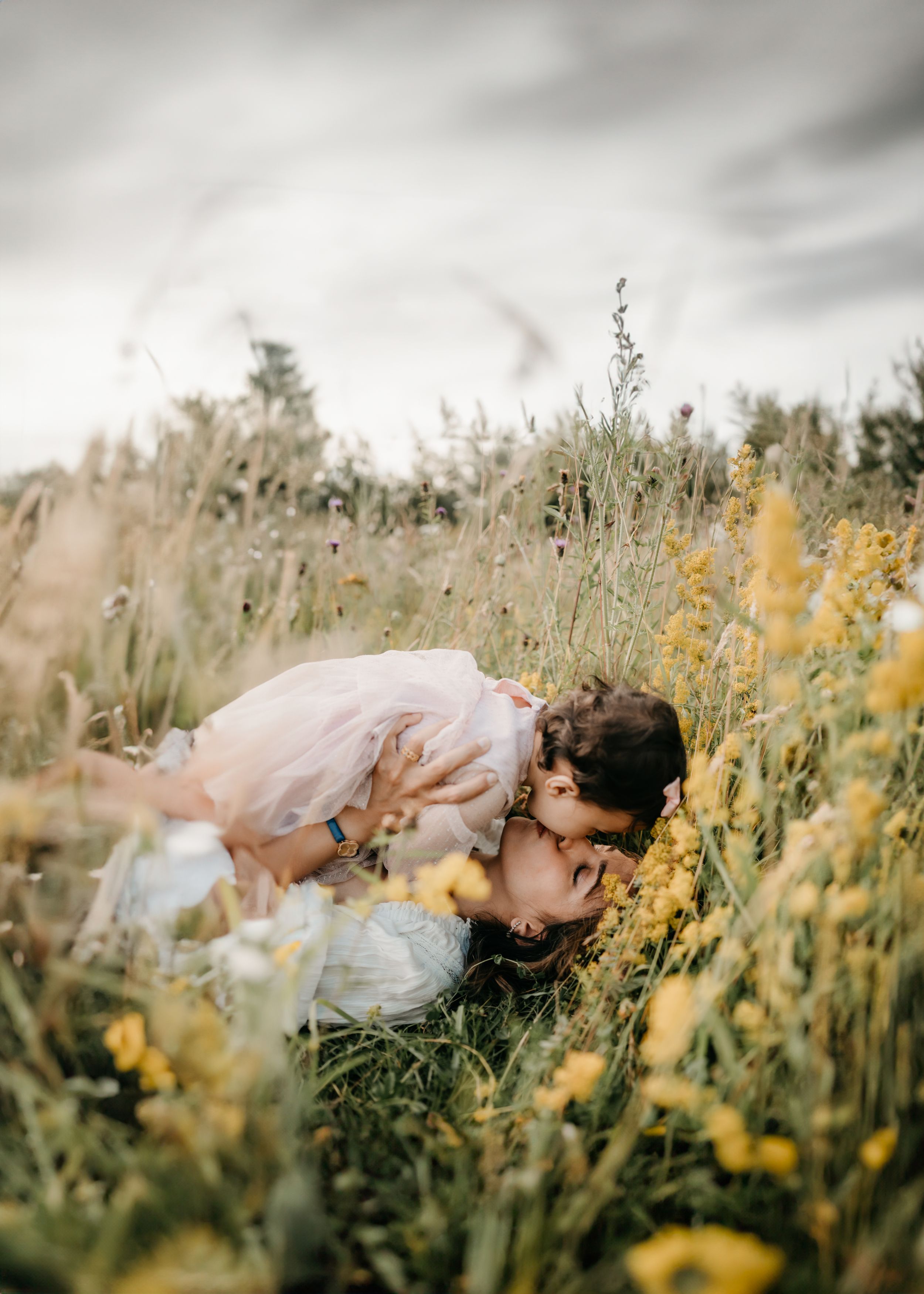 A mother kissing her daughter in a field of flowers during a family photo session in Kent