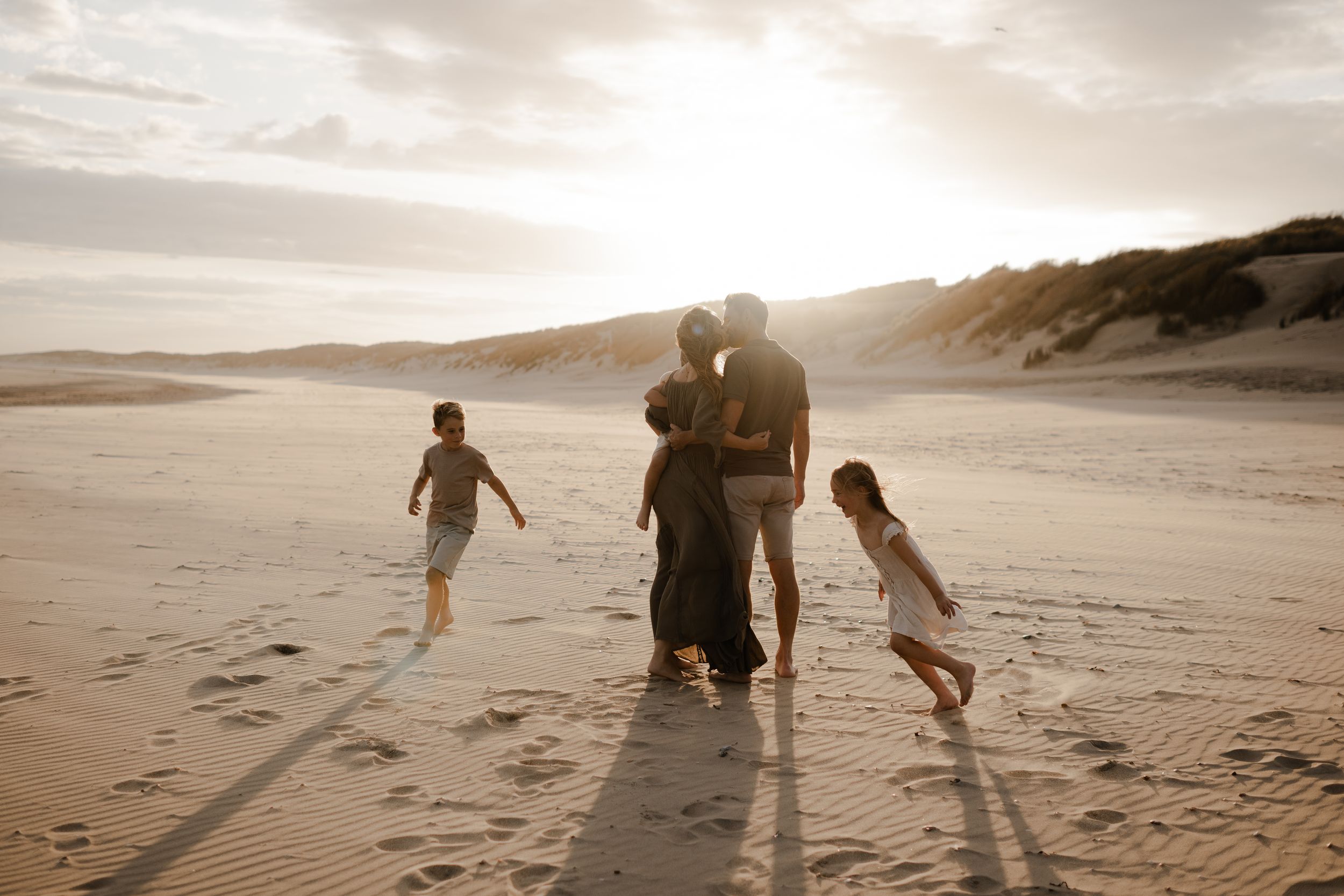 a couple kissing while their children run around them on the beach during their kent family photo session