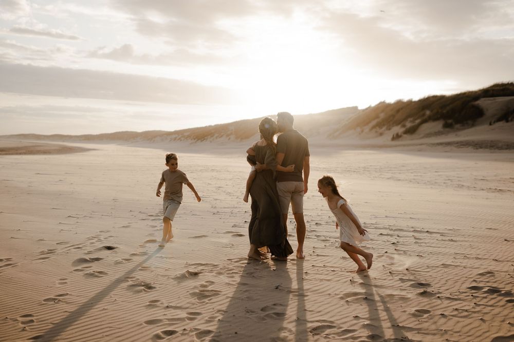 a couple kissing while their children run around them on the beach during their kent family photo session