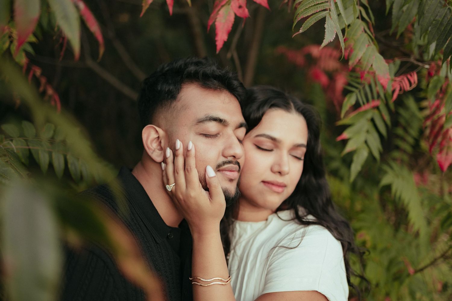 Intimate moment between couple against red autumn foliage.