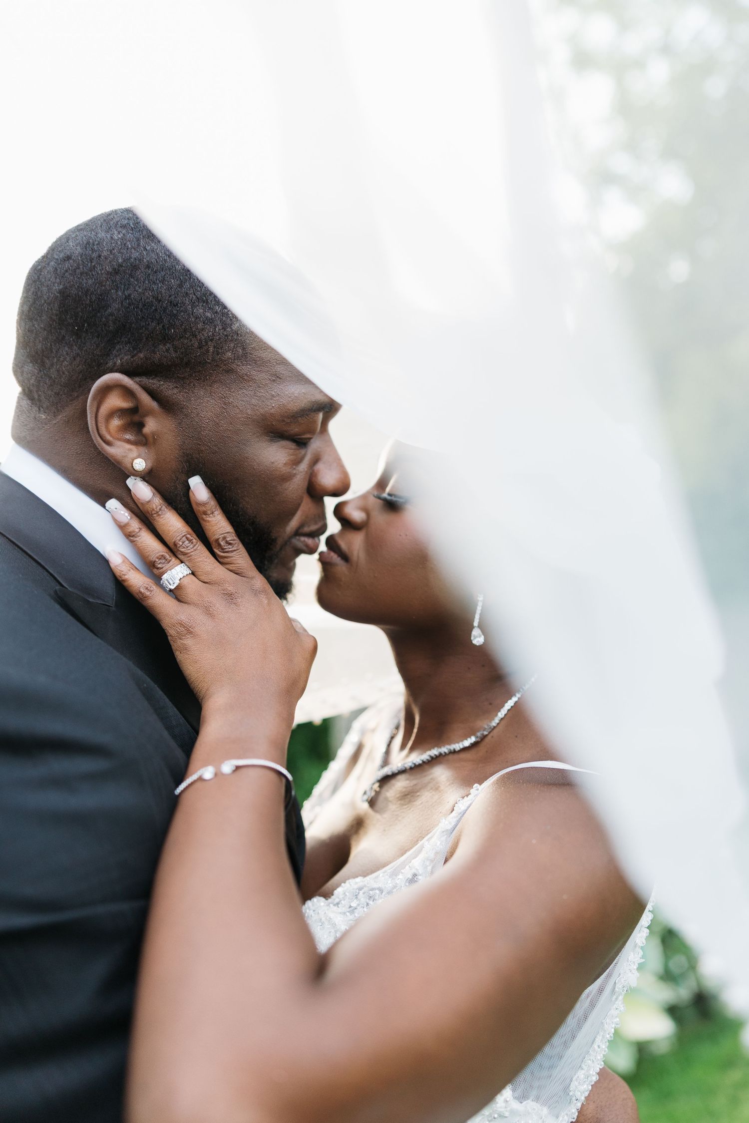 Black bride and groom share a romantic kiss under a flowing white veil on their wedding day.