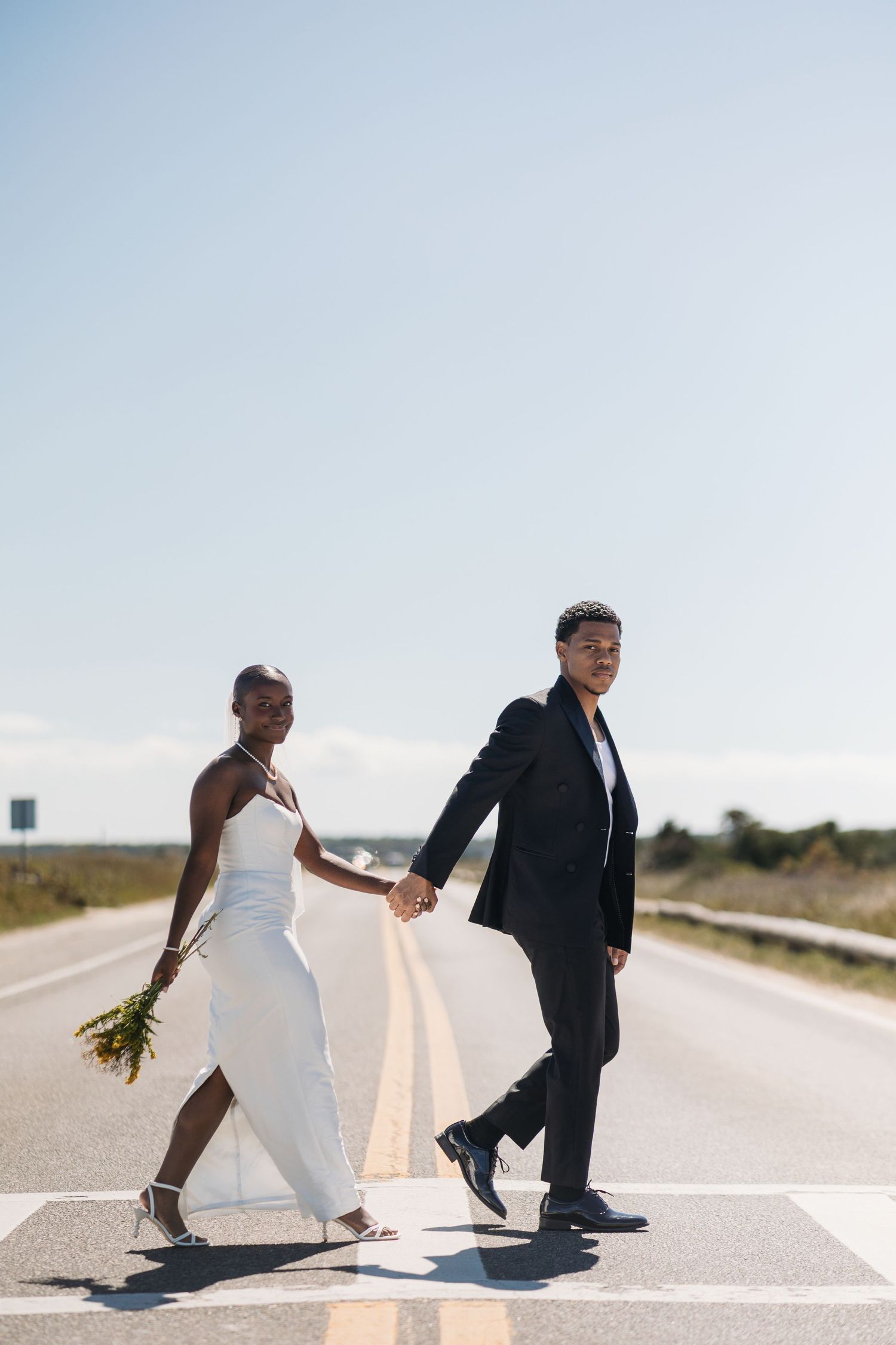 A couple in wedding attire sits on a road in a creative series of minimalist poses at sunset.