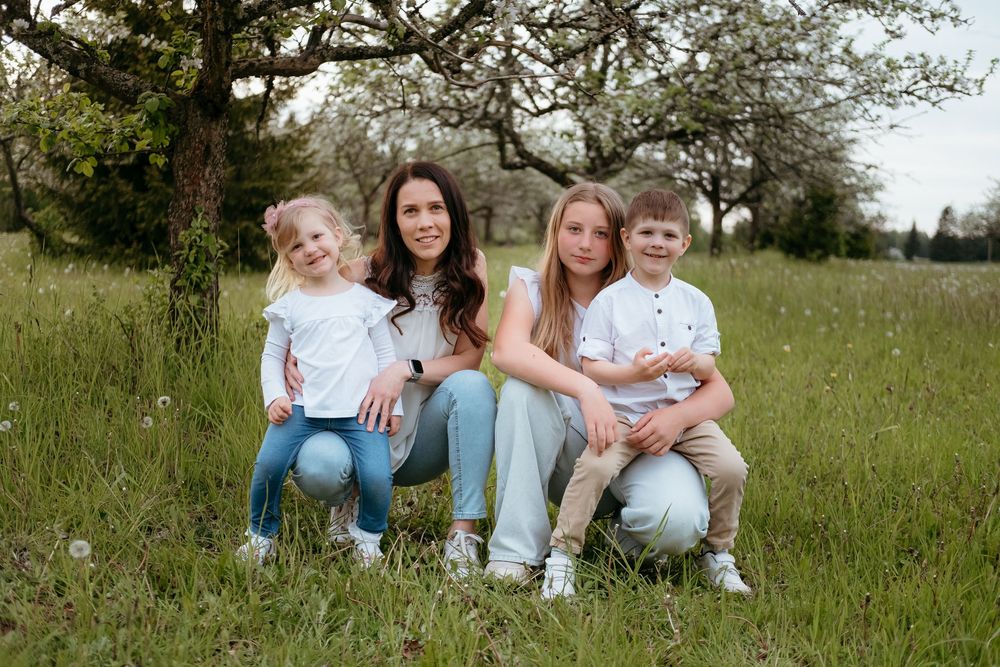 A group sits together in a grassy meadow with oak trees in the background on a sunny day.