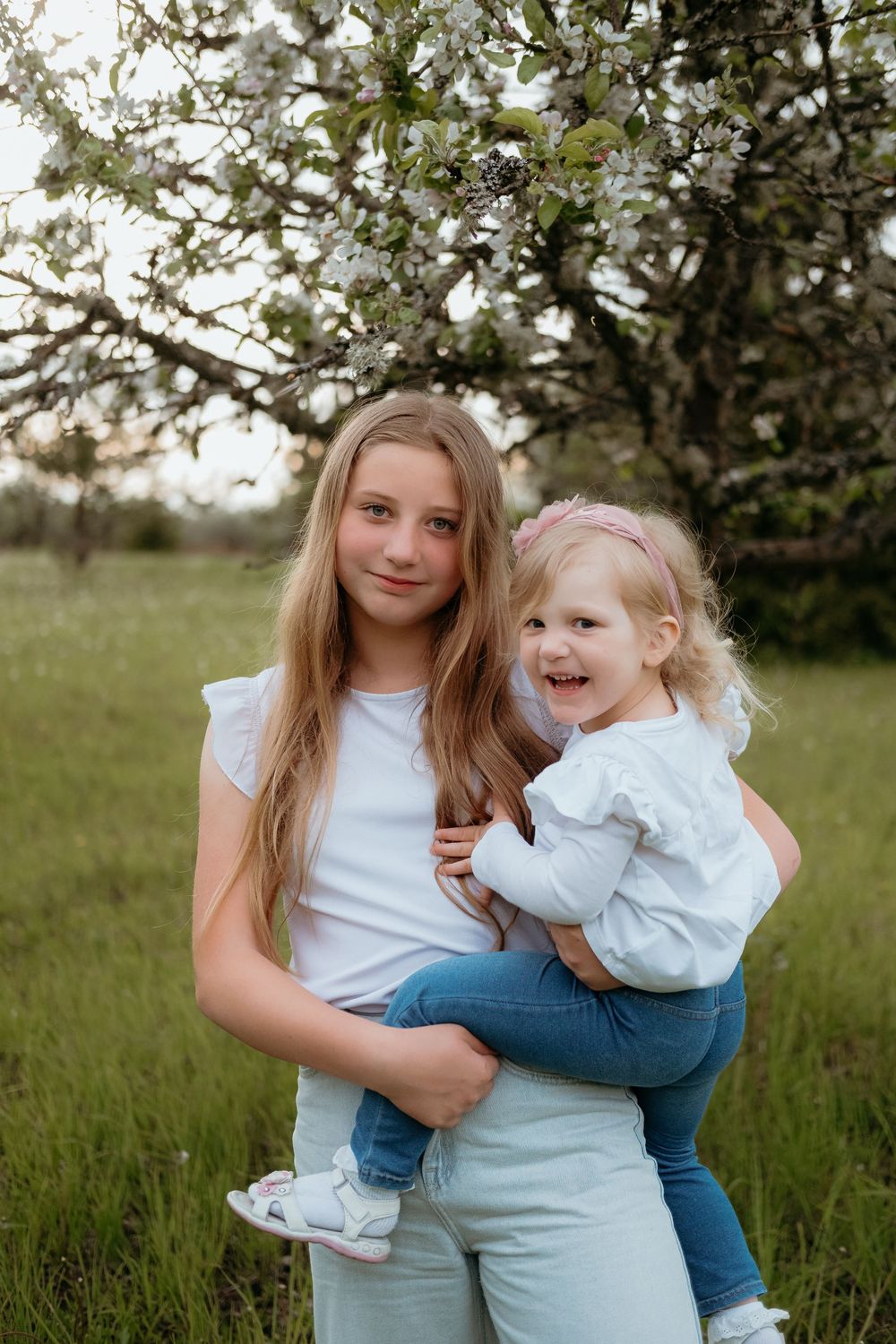 Two people share joyful moments together in a sunny field with blooming trees in the background.