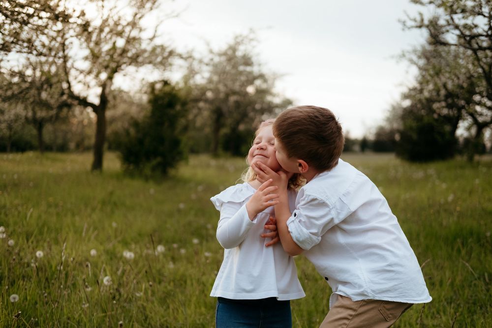 Two people in white shirts share a tender embrace in a grassy meadow during golden hour.