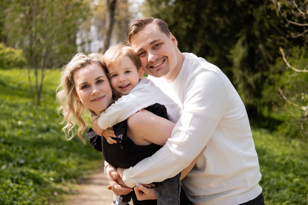 Family embracing outdoors in a natural setting with green trees and foliage in the background.