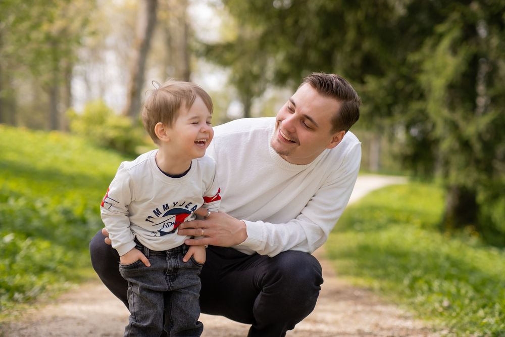 A parent and child share a playful moment together on a path surrounded by lush greenery and flowers.