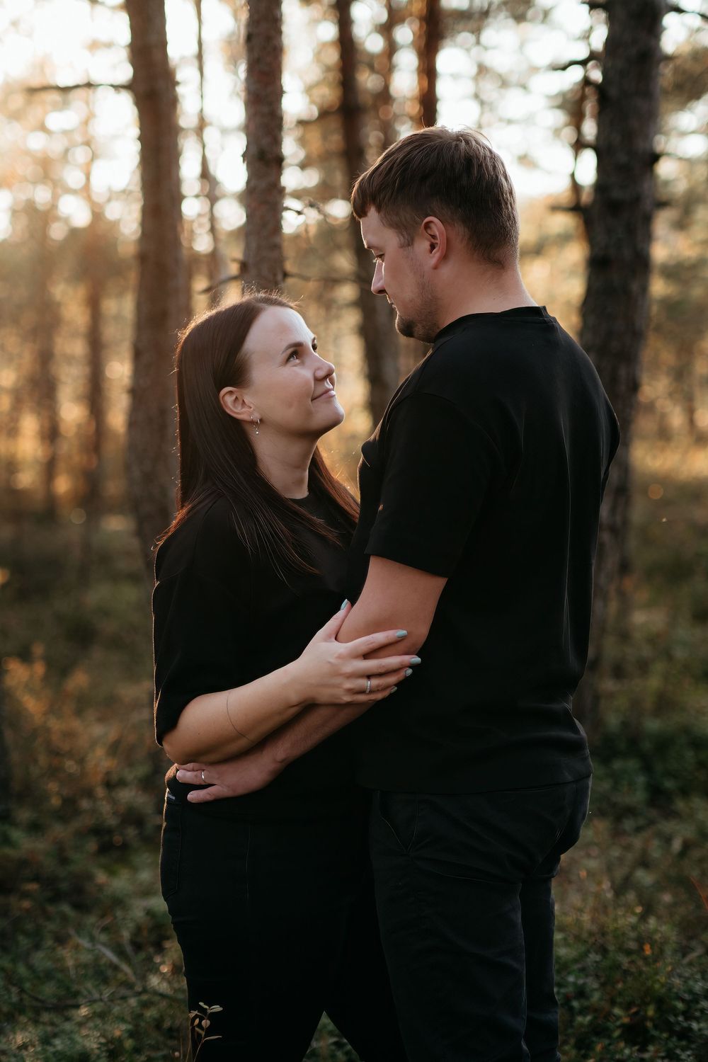 A couple embraces tenderly in a sunlit autumn forest setting with warm golden light filtering through the trees.
