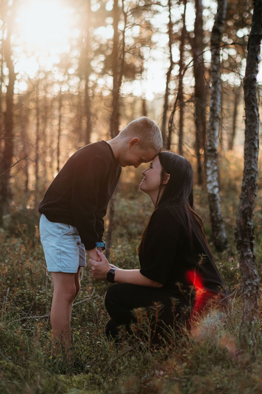 Couple sharing an intimate moment in a sunlit forest with birch trees during golden hour.