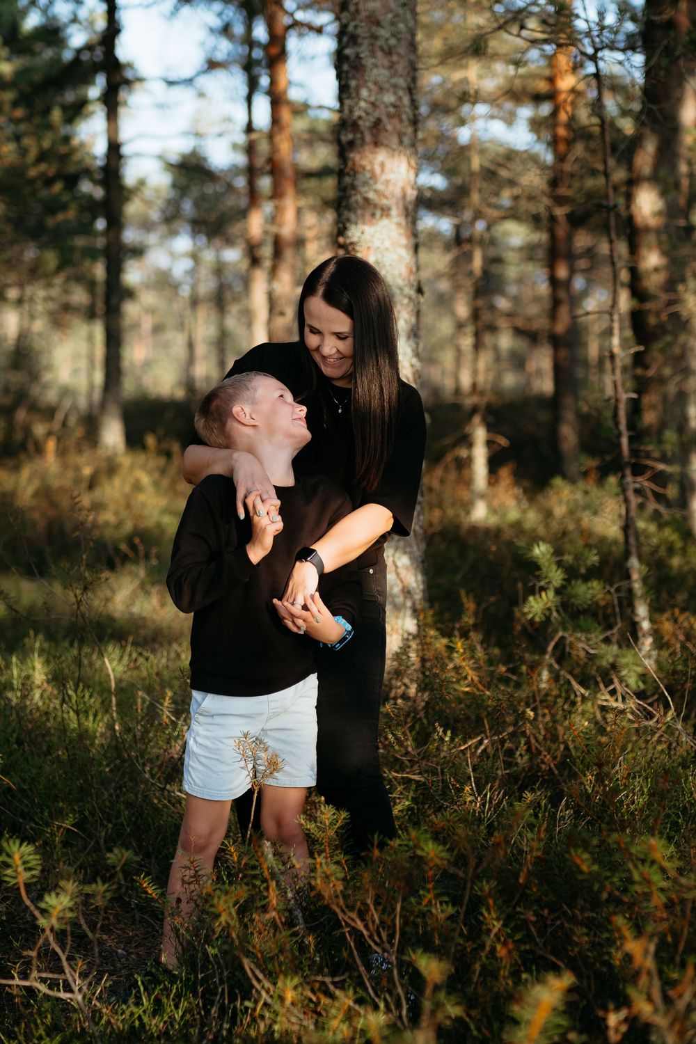 A couple shares tender moments together in a sunlit pine forest setting.
