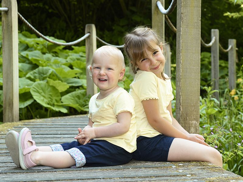 Two children relax on a wooden bridge in a vibrant summer garden in Buckinghamshire, photographed by Abigail's studio.