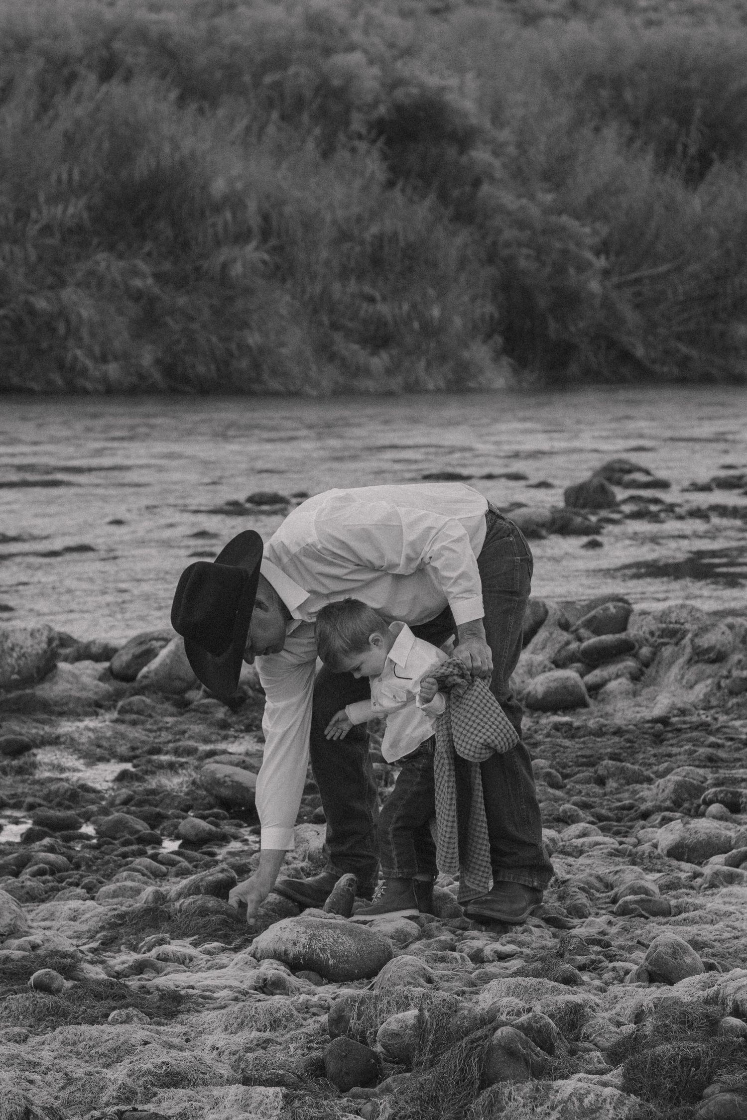A black and white photo of people exploring rocky riverbank together.