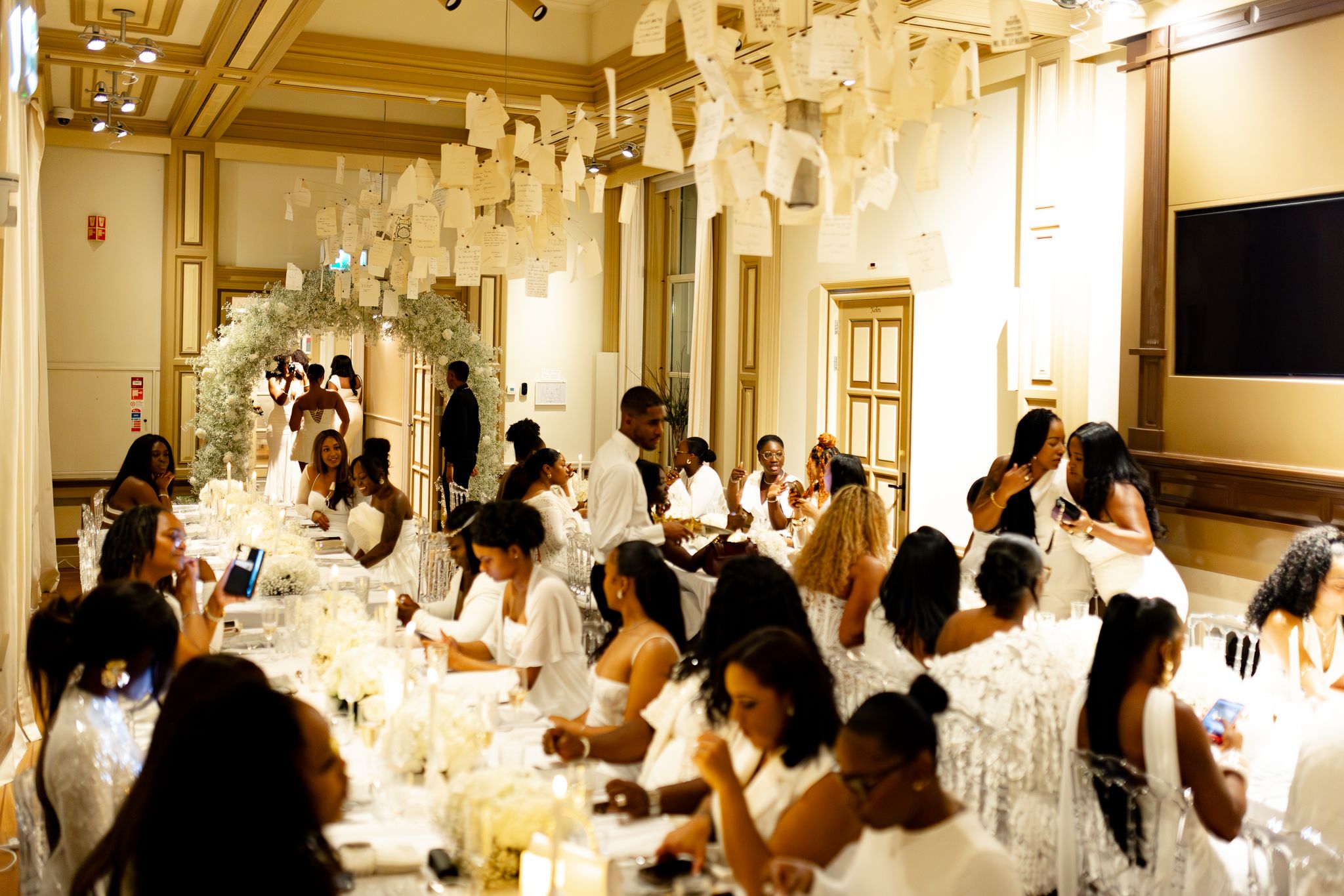 A large banquet hall set for an elegant wedding reception with white tablecloths and crystal chandeliers overhead.
