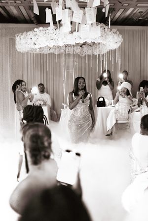 Black and white photograph of guests mingling under crystal chandeliers at an elegant reception venue.