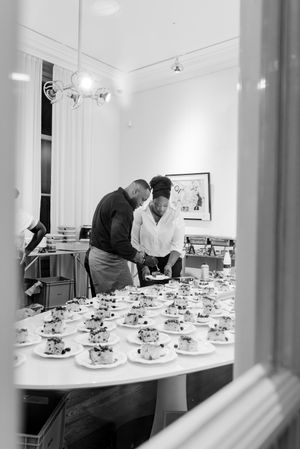 Black and white photo of two people arranging teacups on a large table.
