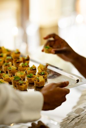 Elegant appetizers arranged on white serving platters with garnishes being carefully plated at an upscale event.