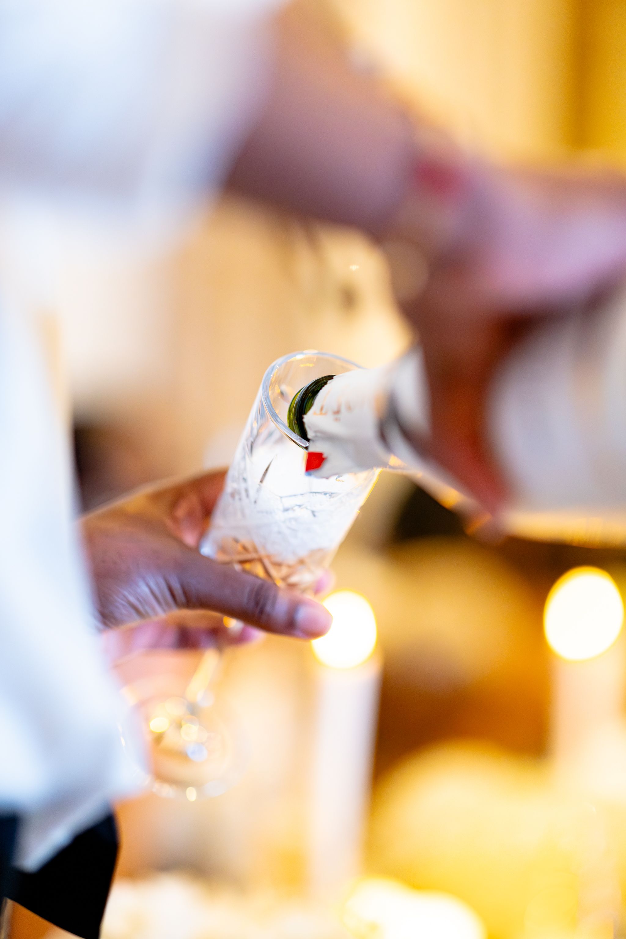Close-up shot of hands pouring white wine into elegant wine glasses at an upscale dining event.