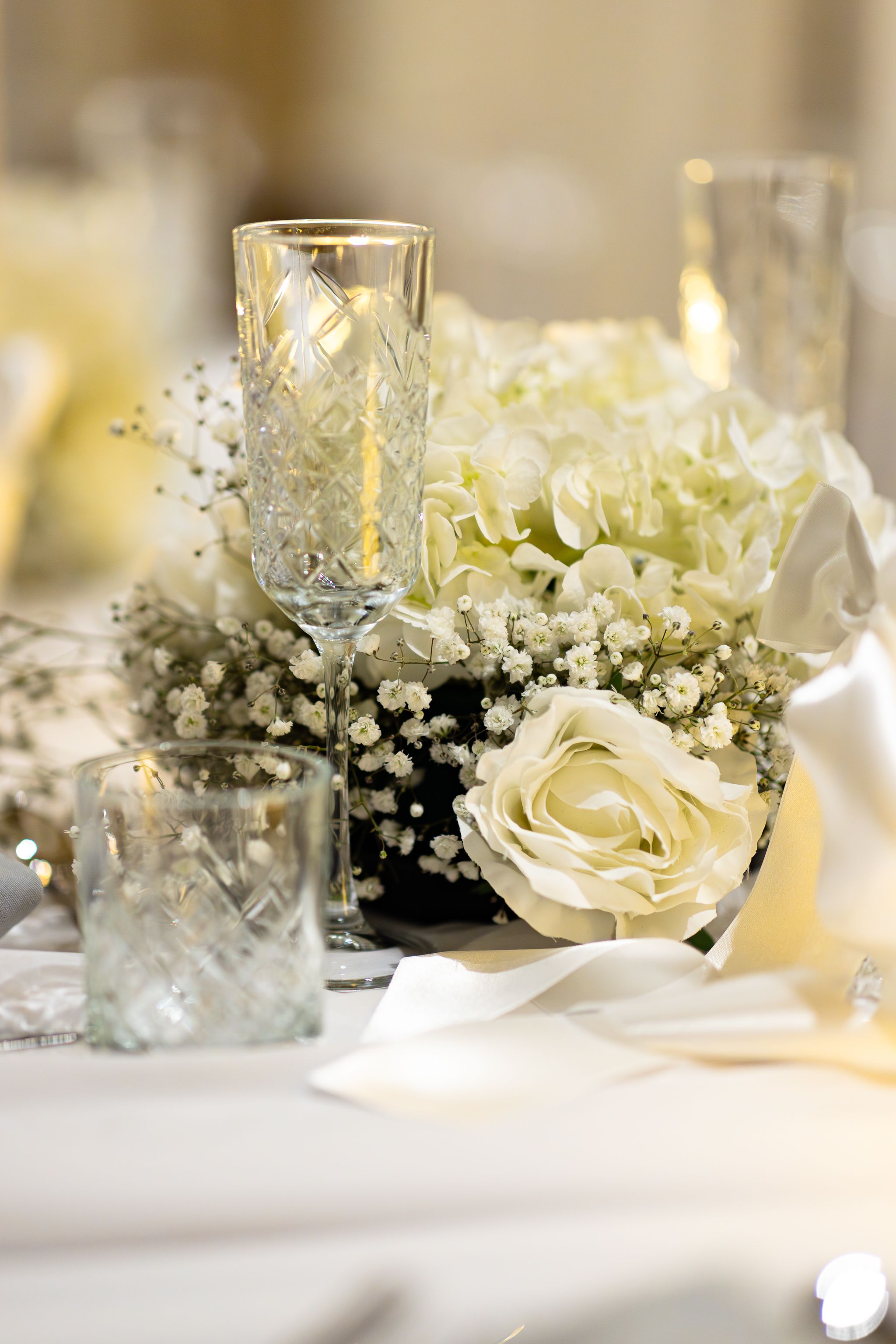 Close-up of delicate white roses and baby's breath floral arrangements on wedding reception tables with candlelight.